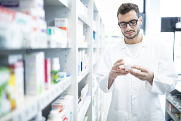 Pharmacist holding product at shelf in pharmacy - WESTF23934