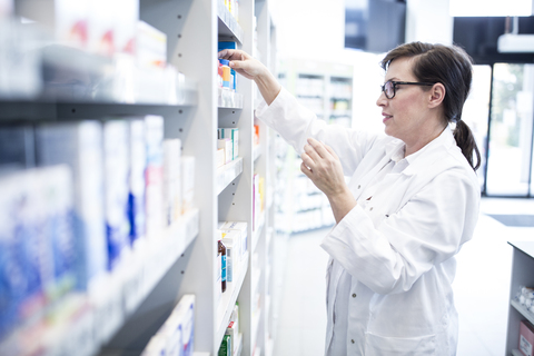 Pharmacist sorting medicine at shelf in pharmacy stock photo