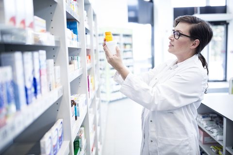 Pharmacist holding product at shelf in pharmacy stock photo