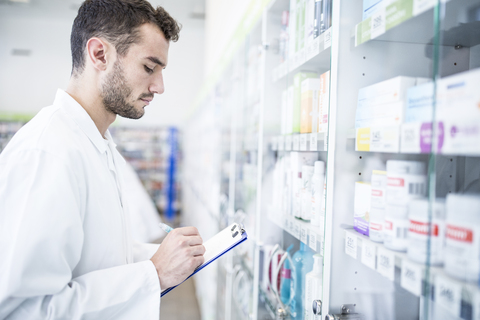 Pharmacist holding clipboard at shelf in pharmacy stock photo