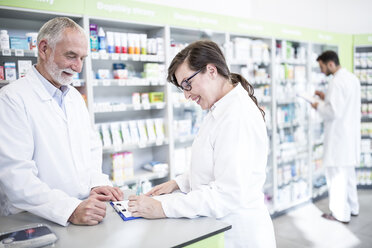 Two smiling pharmacists with clipboard at counter in pharmacy - WESTF23980