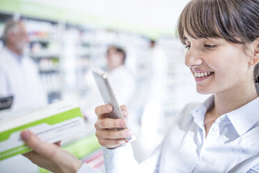 Smiling woman in pharmacy holding smartphone and medicine - WESTF23983