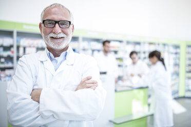 Portrait of smiling pharmacist in pharmacy with colleagues in background - WESTF23988