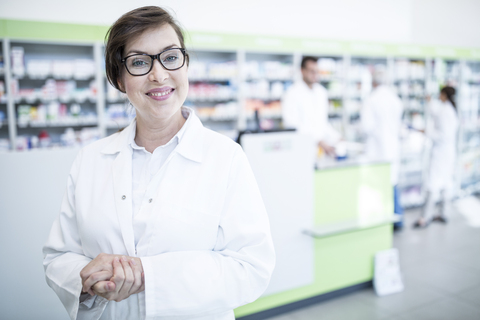 Portrait of smiling pharmacist in pharmacy with colleagues in background stock photo