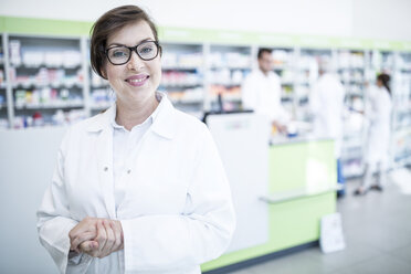 Portrait of smiling pharmacist in pharmacy with colleagues in background - WESTF23989