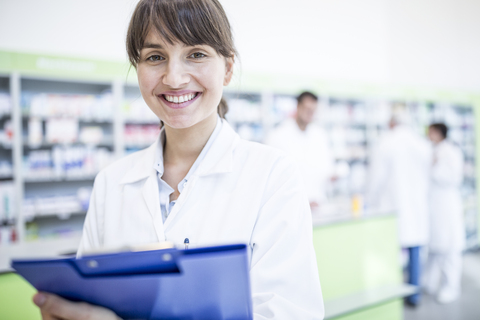 Porträt einer lächelnden Apothekerin in einer Apotheke mit einem Klemmbrett, lizenzfreies Stockfoto