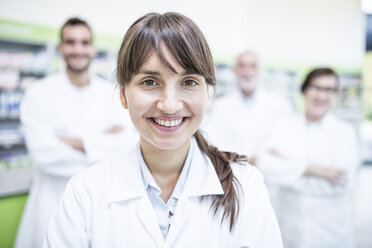 Portrait of smiling pharmacist in pharmacy with colleagues in background - WESTF23991