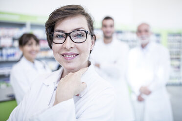 Portrait of smiling pharmacist in pharmacy with colleagues in background - WESTF23992