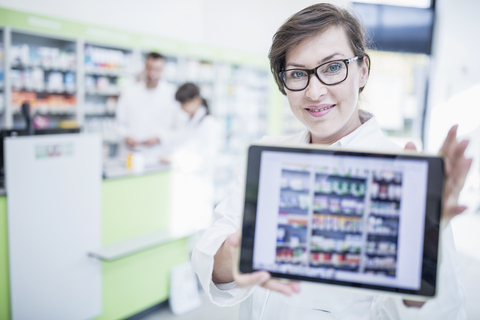 Porträt einer lächelnden Apothekerin in einer Apotheke, die eine Tablet zeigt, lizenzfreies Stockfoto