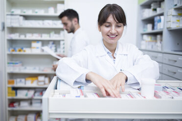 Lächelnder Apotheker, der in einer Apotheke Medikamente aus einem Schrank heraussucht - WESTF23997