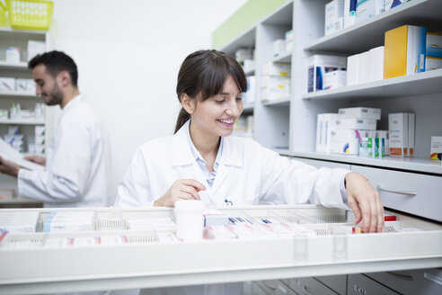 Lächelnder Apotheker, der in einer Apotheke Medikamente aus einem Schrank heraussucht - WESTF23998