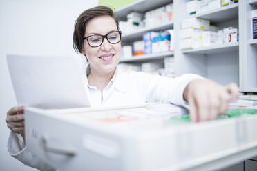 Lächelnder Apotheker, der in einer Apotheke Medikamente aus einem Schrank heraussucht - WESTF24001