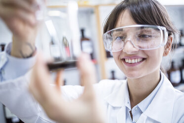 Smiling woman looking at beaker in laboratory - WESTF24017