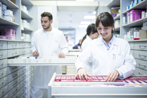 Smiling pharmacist seeking out medicine at cabinet in pharmacy stock photo