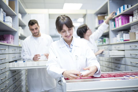 Smiling pharmacist seeking out medicine at cabinet in pharmacy stock photo