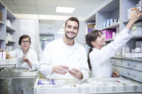 Lächelnde Pharmazeuten bei der Arbeit an einem Schrank in einer Apotheke, lizenzfreies Stockfoto