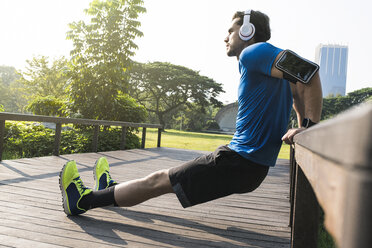 Runner with headphones doing push-ups in urban park - SBOF01112