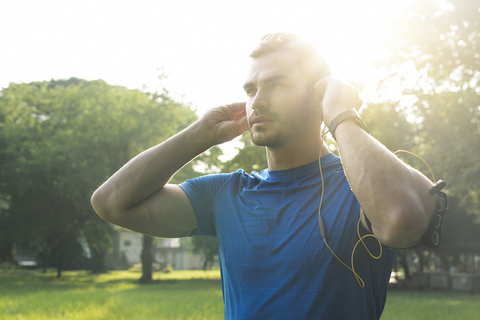 Sportlicher Mann mit Kopfhörern, der sich auf ein Training im Stadtpark vorbereitet, lizenzfreies Stockfoto