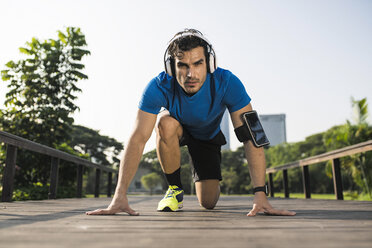 Runner training start position on street in urban park, wearing headphones - SBOF01128