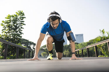 Läufer trainiert Startposition auf der Straße im Stadtpark, trägt Kopfhörer - SBOF01129