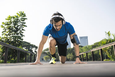 Runner training start position on street in urban park, wearing headphones - SBOF01129