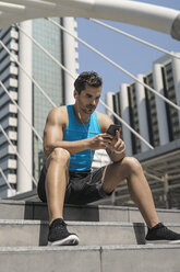 Runner wearing earphones, checking messages on his smartphone - SBOF01151