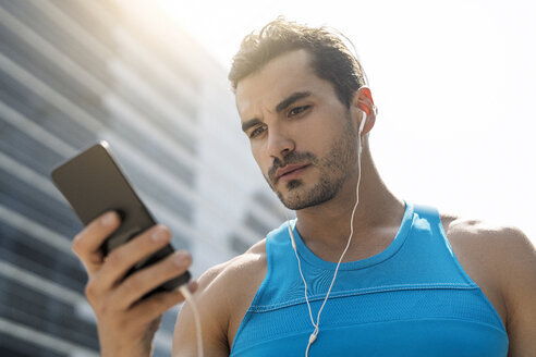 Läufer mit Kopfhörern, der Nachrichten auf seinem Smartphone abruft - SBOF01152