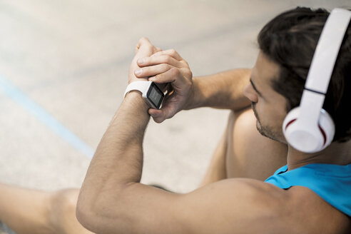 Sportler mit Kopfhörern, der auf dem Boden sitzt und seine Smartwatch überprüft - SBOF01161