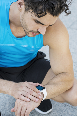 Sportler, der auf dem Boden sitzt und seine Smartwatch überprüft, lizenzfreies Stockfoto