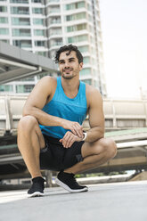 Man in blue fitness shirt kneeling on the ground in city - SBOF01166