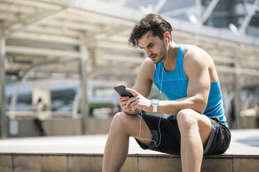 Runner wearing earphones, checking messages on his smartphone - SBOF01169