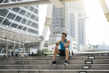 Runner wearing earphones, checking messages on his smartphone - SBOF01171