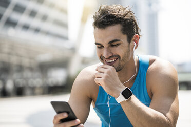 Runner wearing earphones, checking messages on his smartphone - SBOF01172