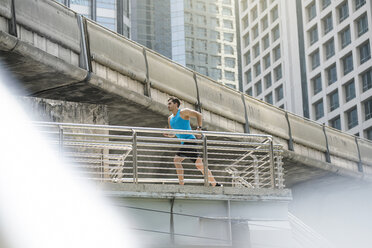 Läufer im blauen Fitness-Shirt läuft über eine moderne Brücke - SBOF01175