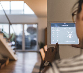 Frau verwendet Bildschirm mit Smart-Home-Steuerungsfunktionen zu Hause - UUF12497