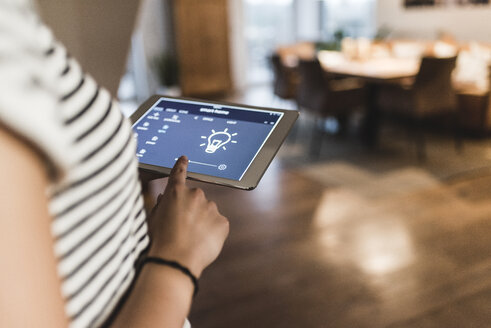 Frau nutzt Tablet mit Smart-Home-Steuerungsfunktionen zu Hause - UUF12499