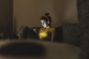 Woman with headphones listening to music on couch at home - UUF12510