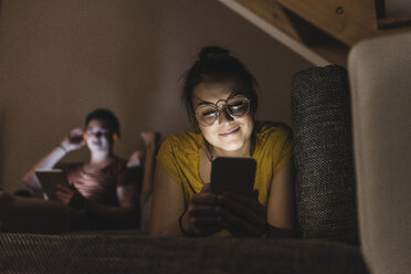 Couple with cell phone and tablet relaxing on couch at home - UUF12514