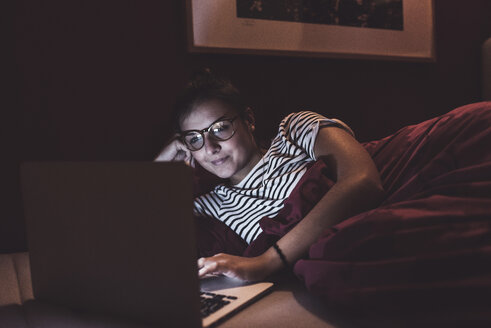 Frau liegt zu Hause im Bett und benutzt einen Laptop - UUF12518