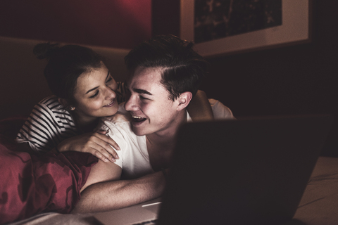 Glückliches Paar im Bett liegend zu Hause mit Laptop, lizenzfreies Stockfoto