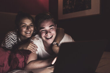 Glückliches Paar liegt zu Hause im Bett und schaut auf den Laptop - UUF12522