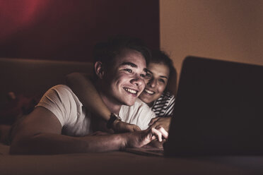 Glückliches Paar liegt zu Hause im Bett und schaut auf den Laptop - UUF12523