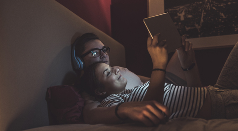 Paar liegt zu Hause im Bett und teilt sich ein Tablet, lizenzfreies Stockfoto