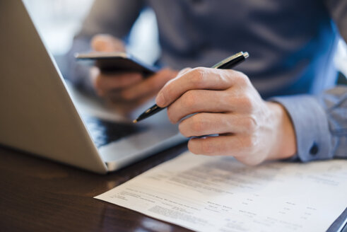 Man at desk using cell phone and holding ball pen in his hand, close-up - DIGF03220