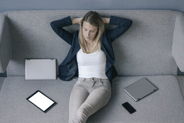 Businesswoman sitting on the couch with several electronic devices relaxing - JOSF02092