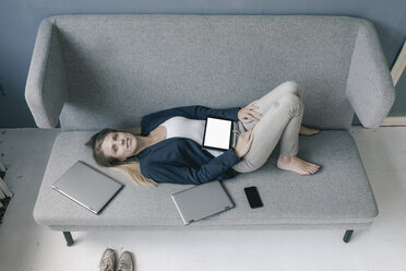 Geschäftsfrau liegend auf der Couch mit mehreren elektronischen Geräten - JOSF02095