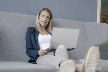 Portrait of pensive businesswoman sitting on couch with laptop - JOSF02097