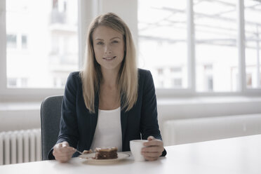 Porträt einer lächelnden Geschäftsfrau bei Kaffee und Kuchen am Schreibtisch im Büro - JOSF02101