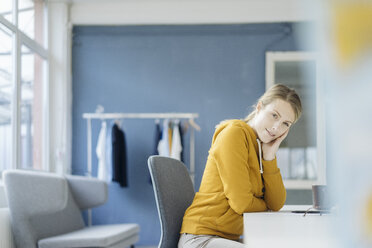 Portrait of fashion designer sitting at desk in her studio - JOSF02122
