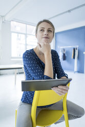 Porträt einer jungen Frau mit Tablet, die auf einem Stuhl in einem Loft sitzt - JOSF02139